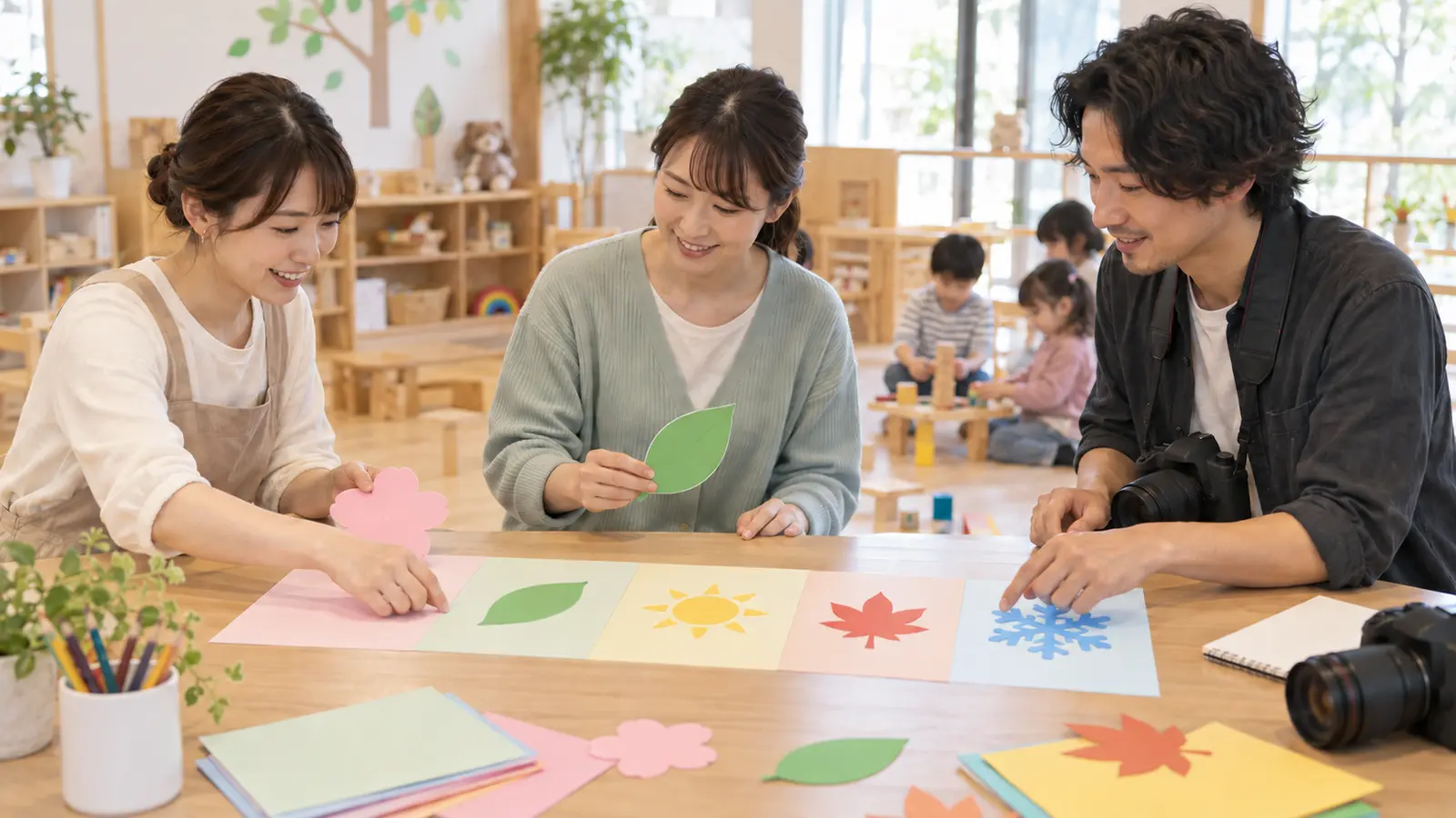 保育室で先生たちが季節のカードを並べて年間の撮影予定を整理する場面