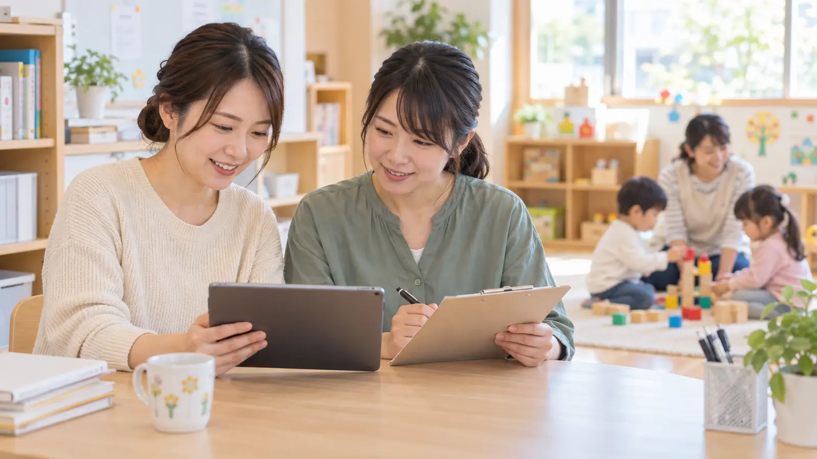 保育室で先生同士がタブレットと確認表を見ながら写真販売の準備をする場面